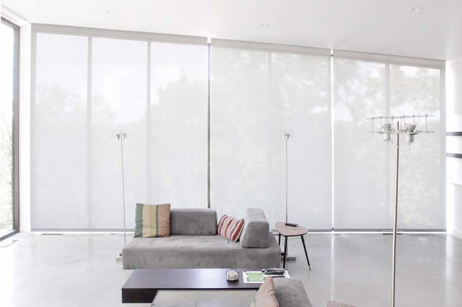 Motorized window shades make controlling natural light effortless in your Destin great room. White motorized shades on a wall of tall great room windows