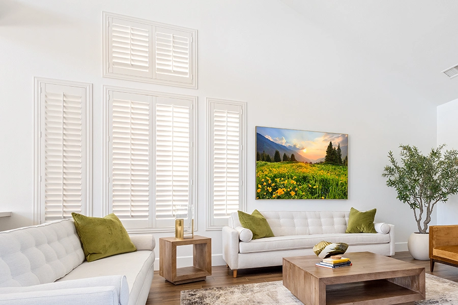 Indoor shutters give you many options for controlling light and privacy. White Polywood shutters on different sizes of windows in a white living room